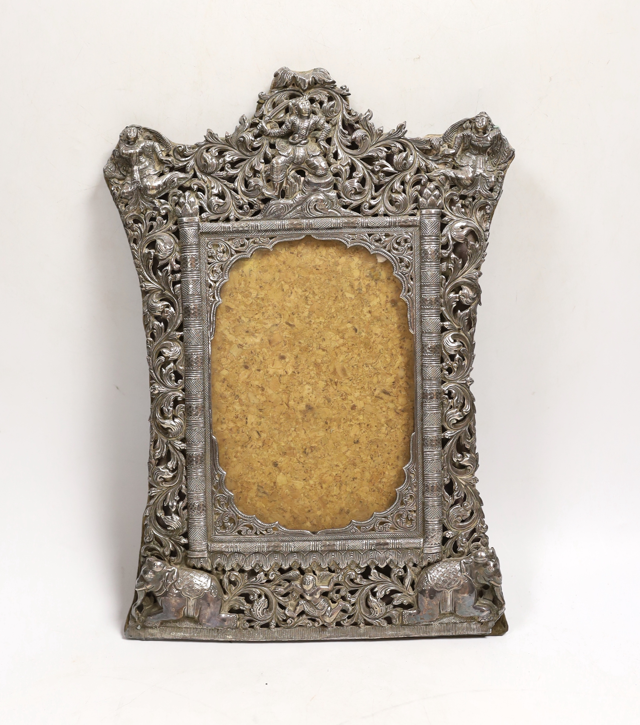 A Burmese white metal mounted shaped rectangular photograph frame, decorated with elephants and figures amongst scrolls, 29.2cm.